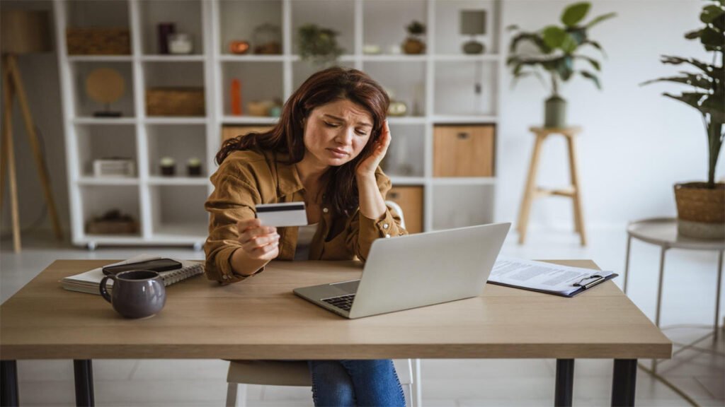 Woman looking stressed while checking credit card and bank balance, showing signs of financial shame